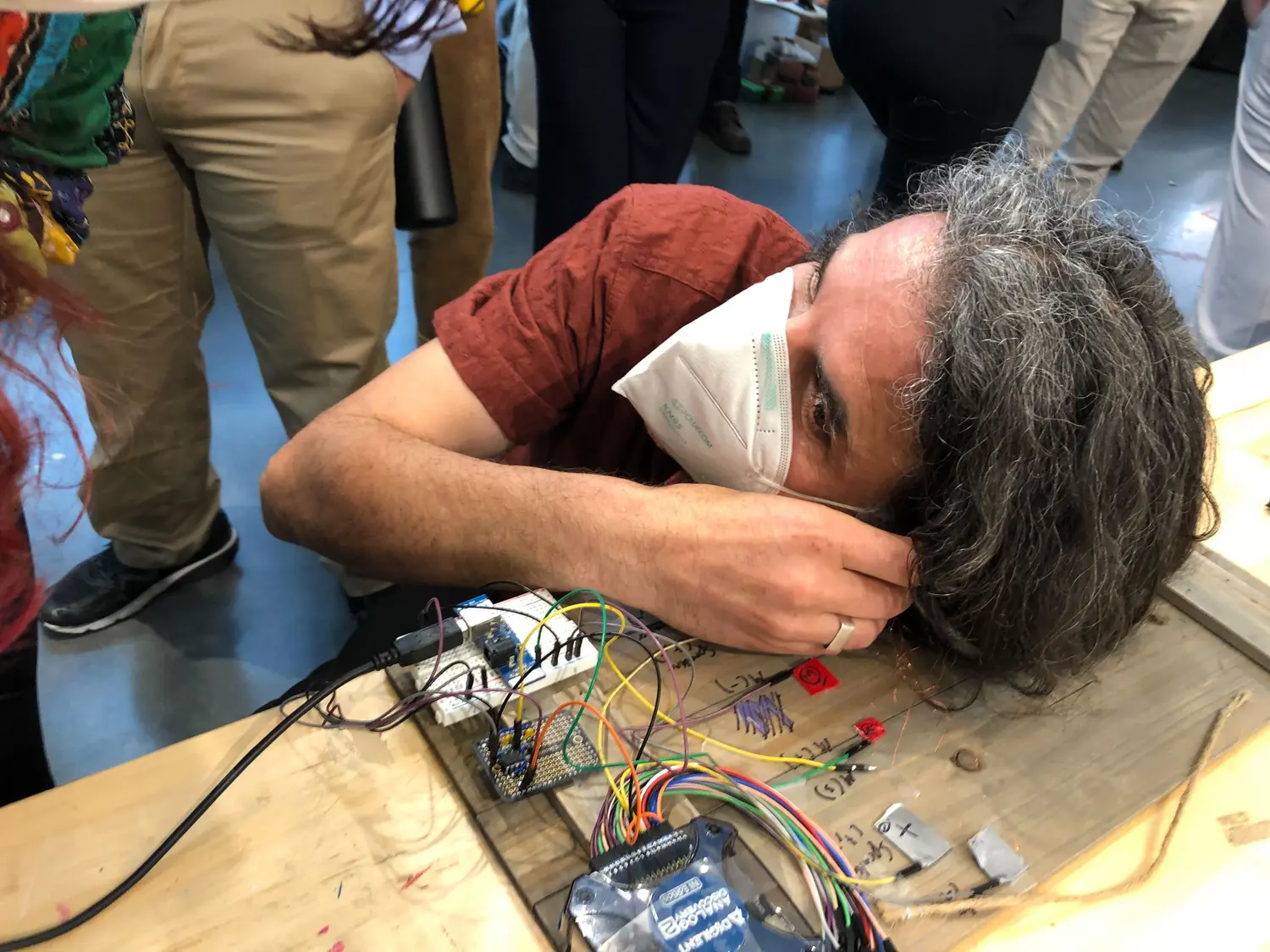 One of our professors testing out the OAE system. Head close to the desk, with the earbud in connected to a mess of wires and circuit boards.