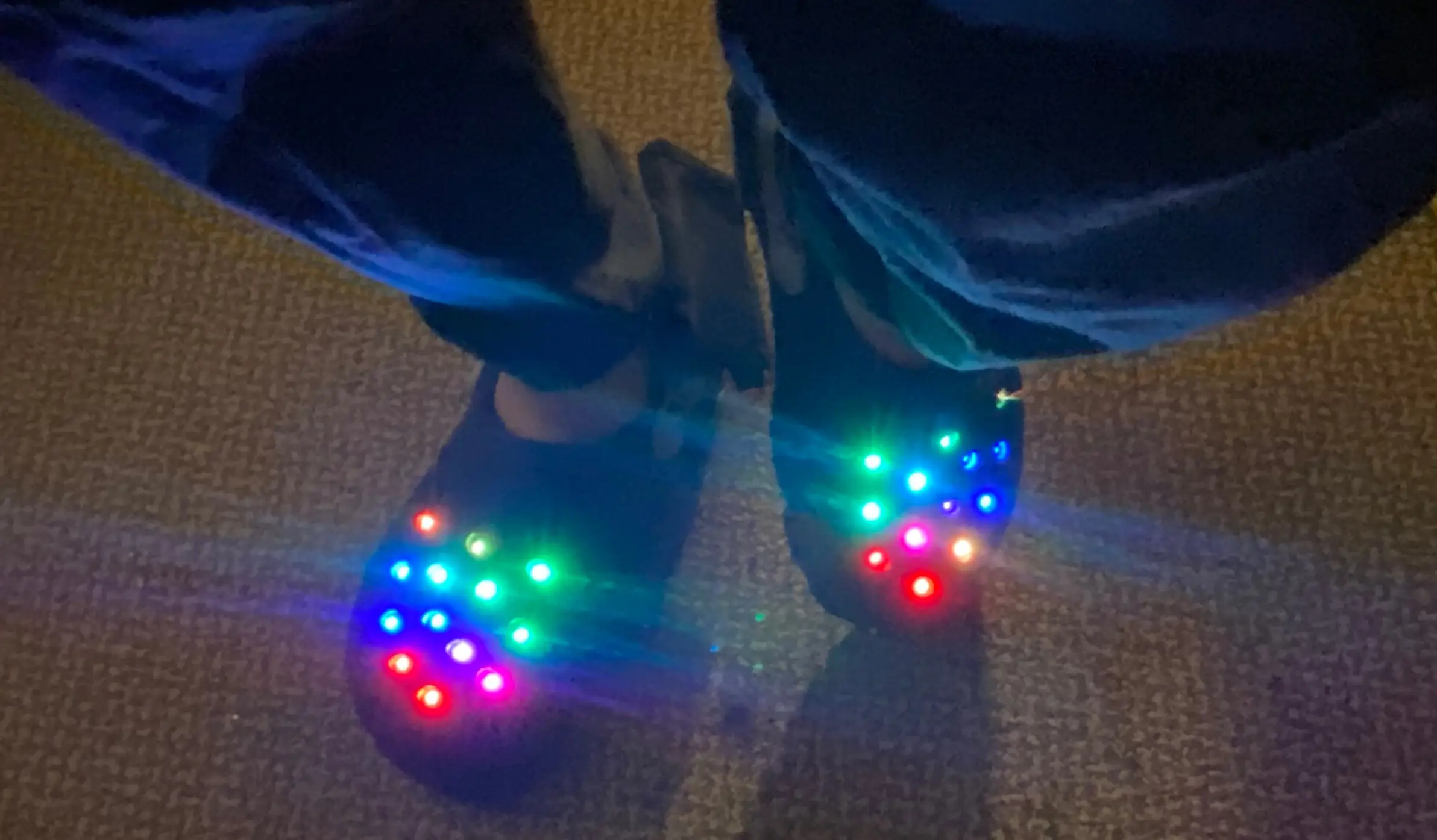 Two feet wearing crocs, the crocs have various color lights emanating from the holes